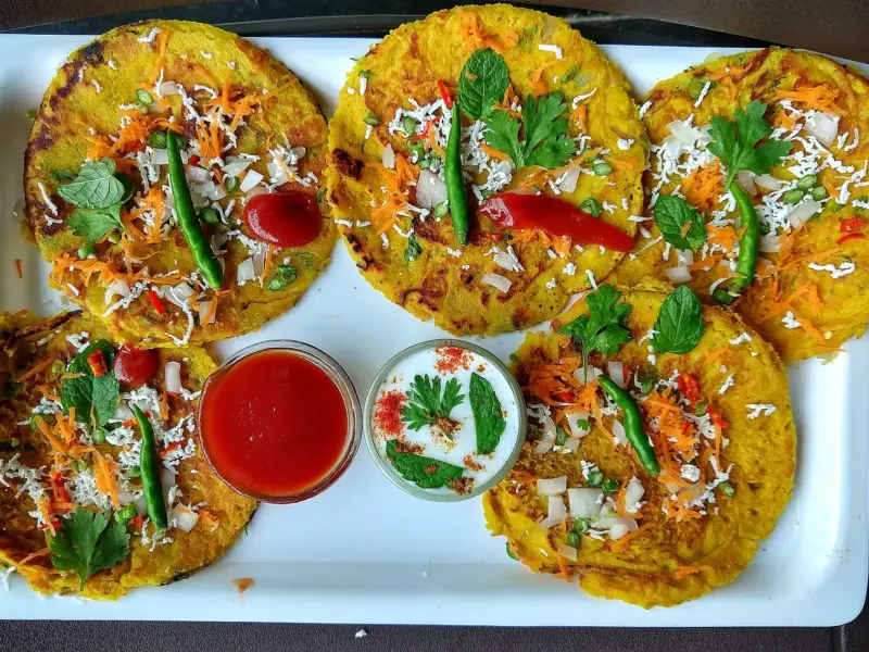 A besan chilla cooking flat in a pan, flecked with onion and coriander.