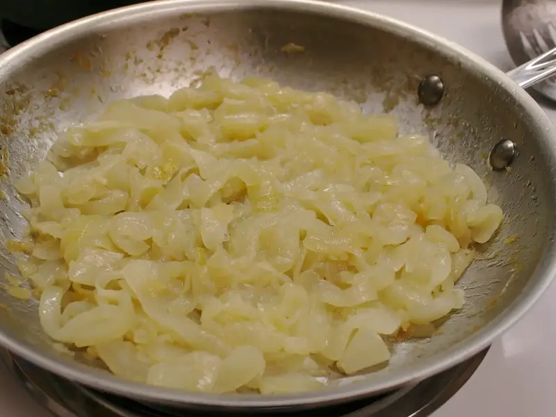 Sliced onions part-way through caramelising in a wide pan.