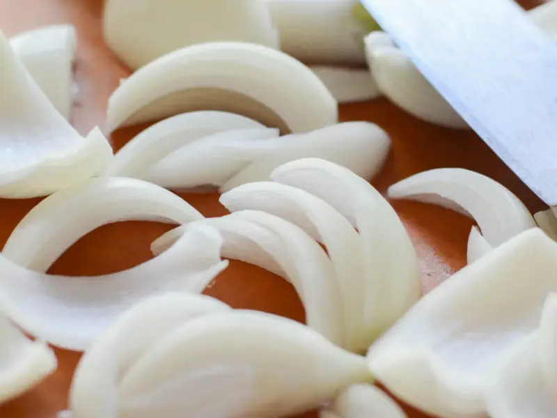 Chopped onion on a wooden board beside a kitchen knife.