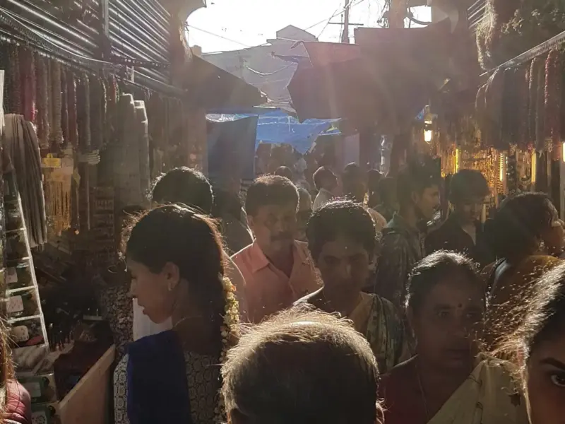 A busy covered market in India with stalls of produce and flowers.