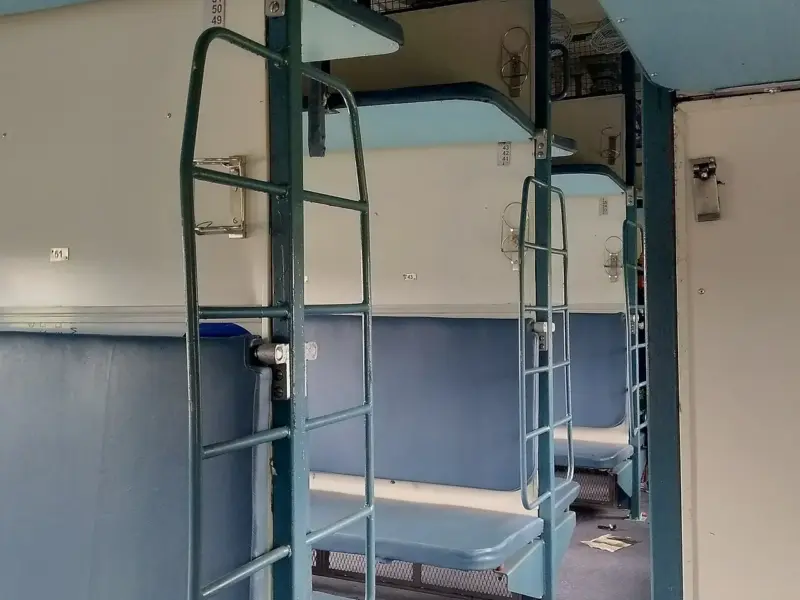 The interior of an Indian Railways sleeper coach with berths on either side of the aisle.