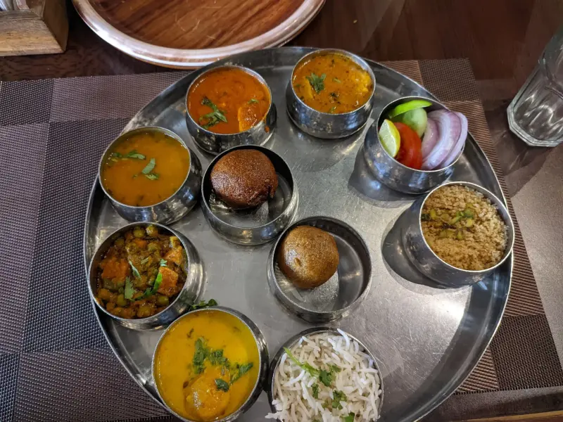 A Rajasthani thali with several small bowls of curries, breads and rice on a metal tray.