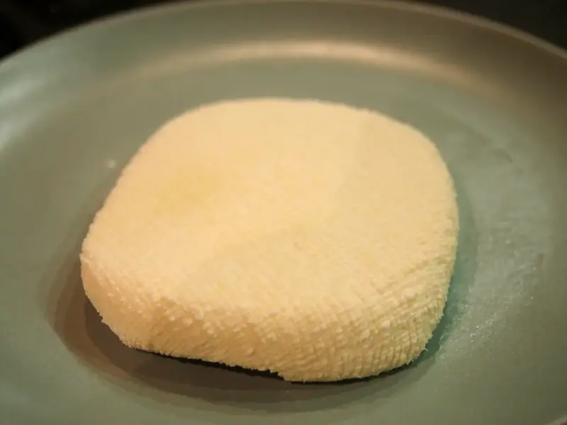 A block of fresh homemade paneer on a board.