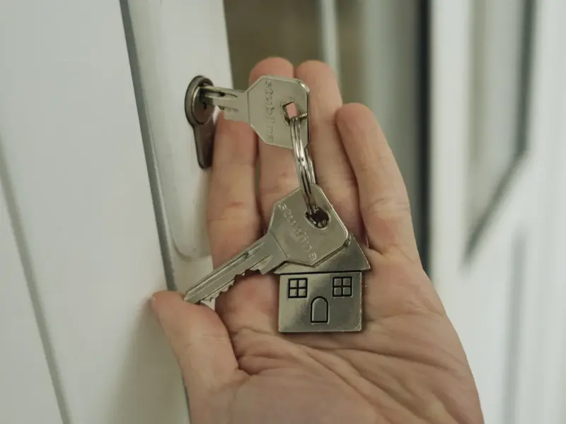A hand holding keys beside a door lock.
