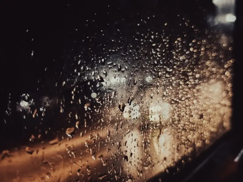 Rain running down a pane of glass at night.