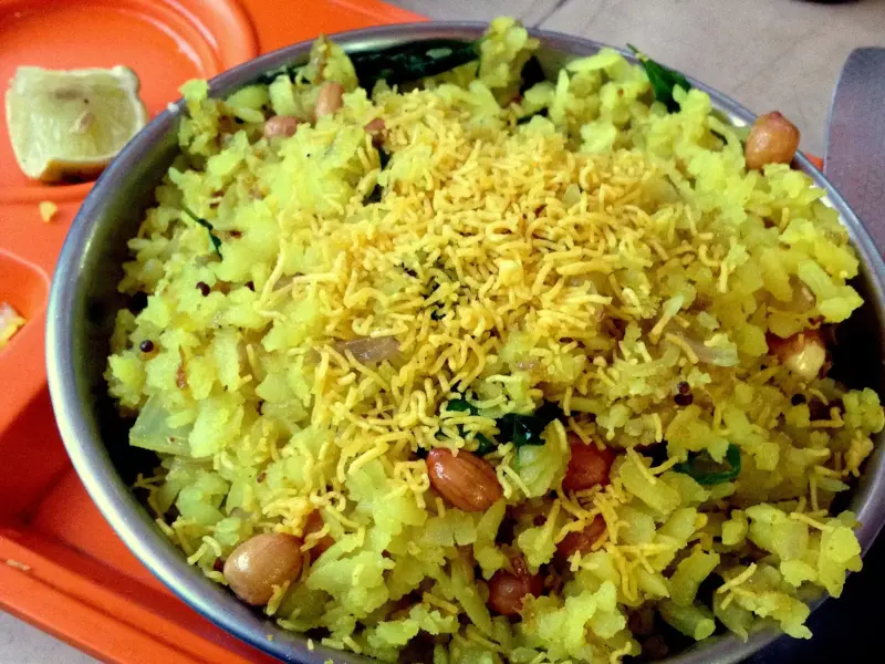 A plate of vegetable poha, yellow with turmeric and scattered with peanuts and coriander.