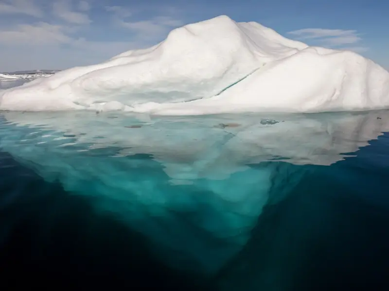 An iceberg in Arctic water with part of its underside visible above the surface.